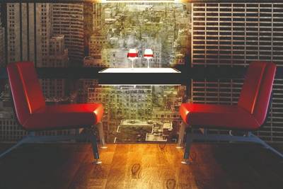 A table set with two wine glasses flanked by two red chairs in front of digitally printed wallpaper showing a cityscape
